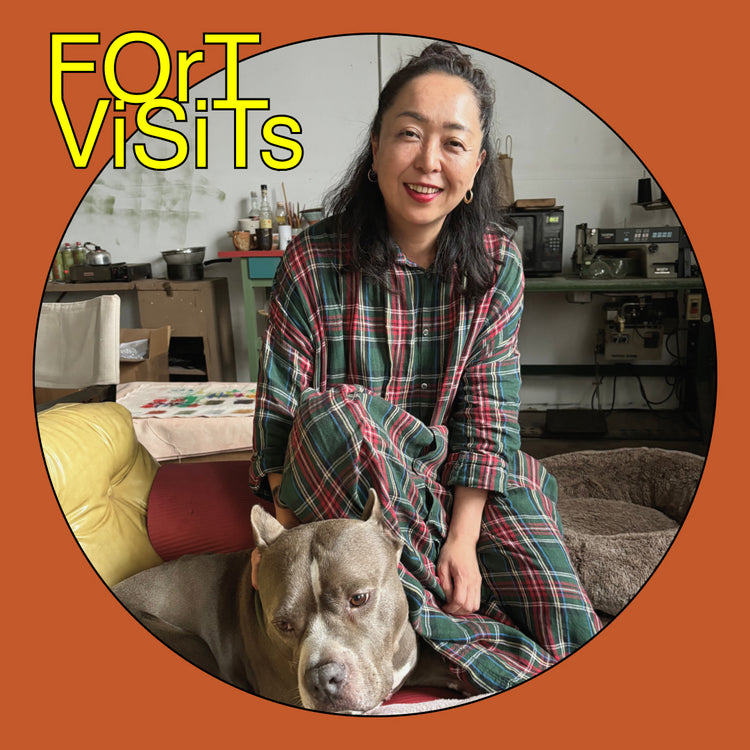 A smiling woman sits indoors with a gray pitbull-type dog on a couch, wearing a green, red, and blue plaid shirt and matching pants. The photo is framed in a circular border with an orange background and the text 'FOR VISITS' in yellow at the top left.