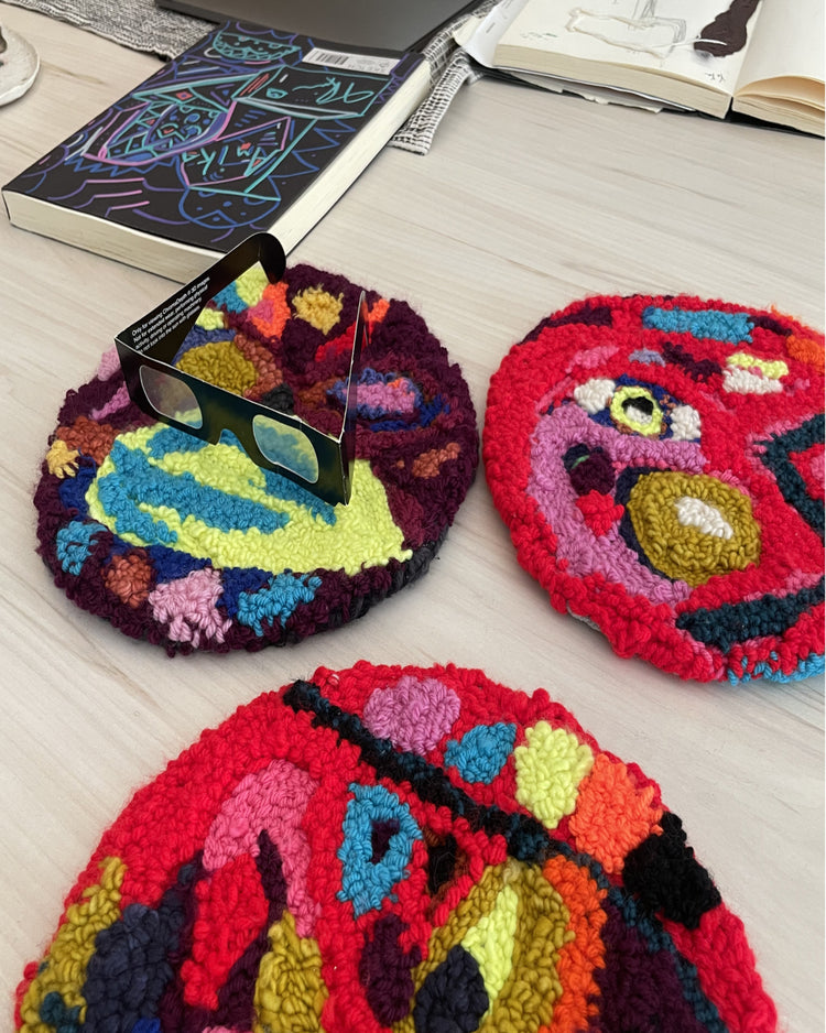 Three colorful hand-tufted wool rugs with abstract patterns are arranged on a light wood floor, alongside a pair of black 3D glasses and books.