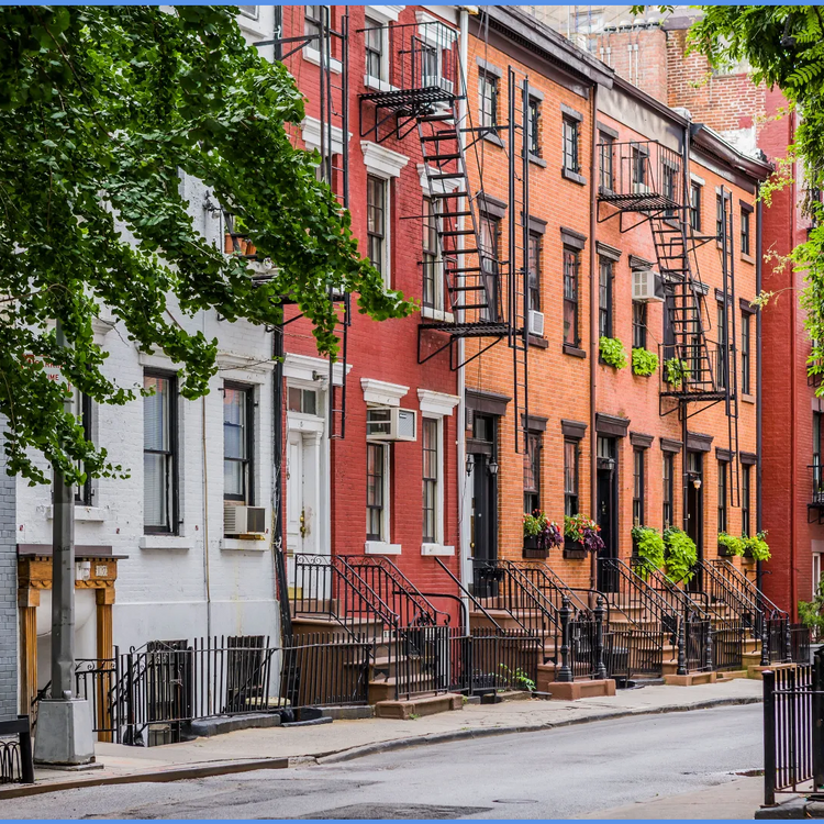 A row of classic urban row houses with red and white brick facades, black fire escapes, front steps, and greenery along the sidewalk and tree canopy.