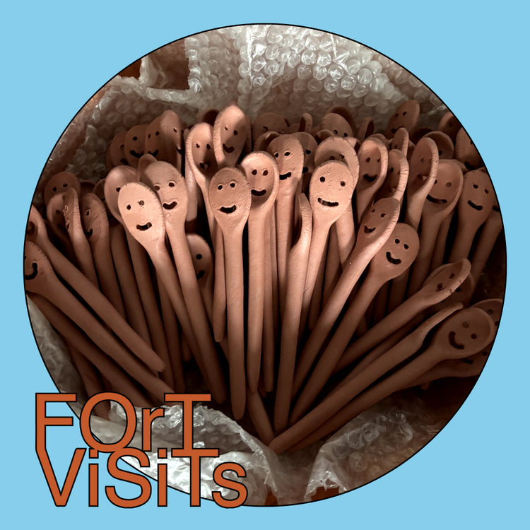 A circular close-up of many small wooden spoon-like utensils with carved smiling faces, packed together on bubble wrap. The image has a light blue border and the text 'For ViSiTs' in orange at the bottom left.