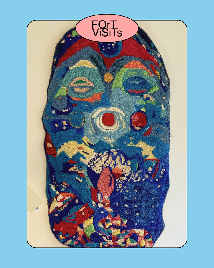A colorful abstract textile wall hanging or tapestry with a stylized face-like composition, featuring blue, red, green, yellow, and white areas. A pink oval sticker reading 'ForI Visits' is placed at the top of the artwork.
