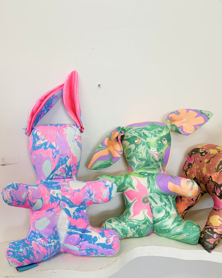 Three colorful, marbled fabric animal-shaped plush toys arranged on a white shelf against a plain light wall.