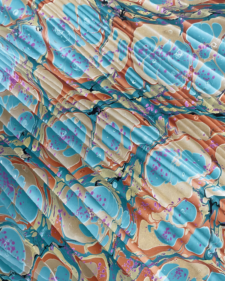 Abstract marbled pattern with flowing organic shapes in turquoise blue, tan, terracotta orange, and small purple accents, filling the full frame.